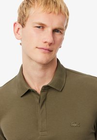 Olivgrön polo med texturerad tyg, med krage och en subtil broderad logo på bröstet.