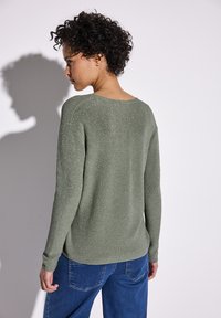 Maglione in maglia verde khaki, luminoso e morbido, con una vestibilità comoda, scollo rotondo e maniche lunghe, abbinato a jeans blu, vista da dietro.