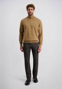 Lichtbruin, gestructureerd sweatshirt met een ritssluiting tot de helft van de kraag, gecombineerd met donkergrijze, aansluitende broeken en bruine schoenen met gespsluiting.