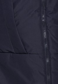 Chaqueta de plumas azul marino con una textura suave y acolchada, cierre de cremallera de longitud completa y detalles de costura horizontal.