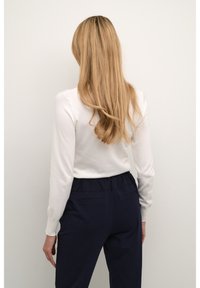 Haut à manches longues blanc avec une texture douce associé à un pantalon bleu marine foncé avec taille élastique et poches arrière.