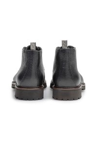 Botines de cuero negro con acabado texturizado, punta redonda, suela marrón de perfil bajo y lengüeta en la parte posterior. Patrón de tracción de goma en la suela.