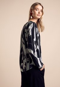 Haut à manches longues avec un motif abstrait en noir et blanc, fabriqué en tissu léger. Il présente une coupe décontractée et un décolleté arrondi.