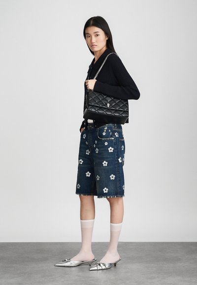 Borsa a tracolla nera trapuntata, maglione scuro, pantaloni shorts in denim con ricami floreali bianchi, mules argentati a punta e calze bianche al ginocchio.