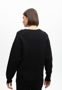 Sudadera negra oversized con cuello redondo, hombros caídos, puños acanalados y dobladillo. Textura suave, diseño minimalista.