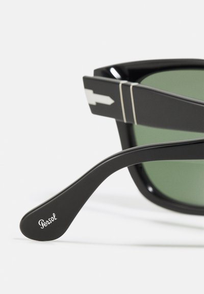 Black Persol sunglasses with green lenses. Thick frame features a white arrow design. Temples have a smooth finish with "Persol" logo.