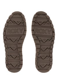 Hnědé gumové podrážky bot s texturovaným gripem, obsahující vyražené logo "ROXY" a výrazné designy připomínající hory.