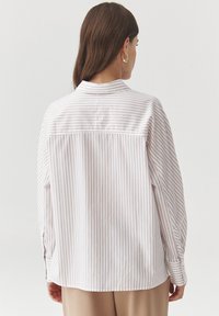 Striped long-sleeve shirt in light pink and white, featuring a back yoke, rounded hem, and button cuffs. Smooth cotton fabric.