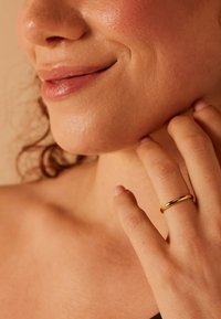Gouden ring om een vinger, gladde textuur, cirkelvormig ontwerp. Close-up van een hand die voorzichtig de kaaklijn aanraakt, met zachte huid en minimale makeup.