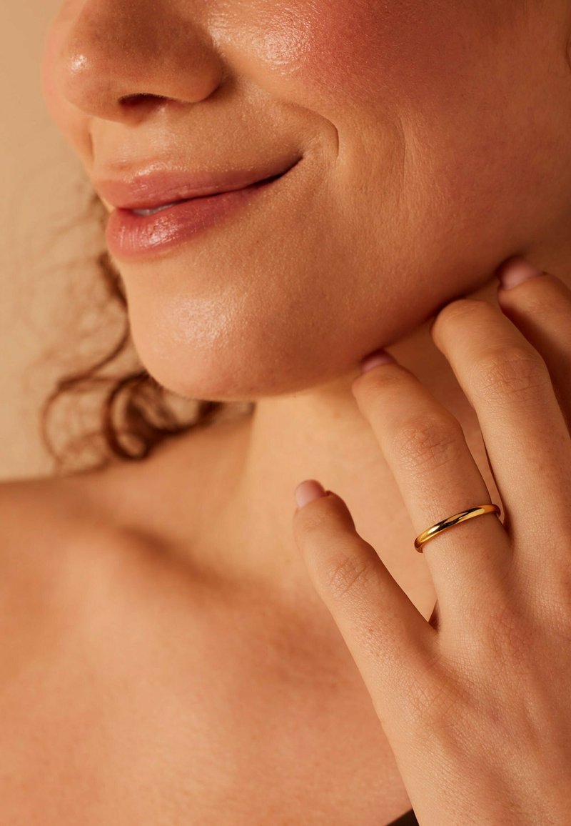 Gouden ring om een vinger, gladde textuur, cirkelvormig ontwerp. Close-up van een hand die voorzichtig de kaaklijn aanraakt, met zachte huid en minimale makeup.