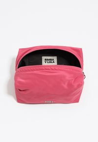 Funda de cremallera rosa parcialmente abierta que muestra un interior negro con la etiqueta "BIMBA Y LOLA" dentro y el logo metálico en la parte frontal.
