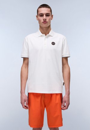 Hvid bomulds polo shirt med et brandet mærke på brystet. Sammen med lys orange shorts, der viser et afslappet, sporty look.