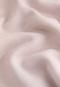 Close-up van zachte, lichtbeige gebreide stof met zichtbare fijne geribde textuur en zachte plooien die gladde schaduwen creëren.