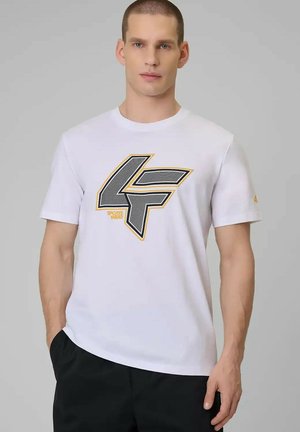 Man met kort haar die een wit T-shirt draagt met een groot zwart-geel "4F" logo, staand tegen een effen grijze achtergrond.