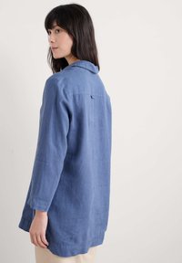 Lichtblauw linnen shirt met lange mouwen, een kraaghals en een relaxte pasvorm. Opvallende kenmerken zijn een rugpand en subtiele stikdetails.