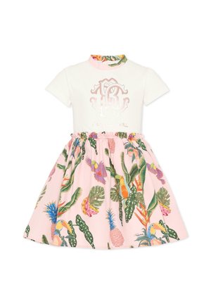 Haut blanc à manches courtes avec logo rose associé à une jupe rose avec un motif feuilles tropicales, fleurs, toucans et ananas.