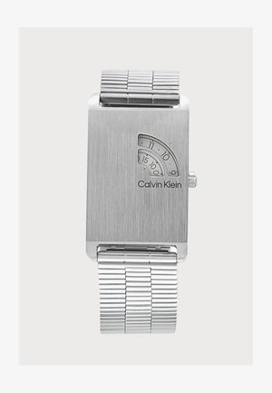 Montre-bracelet argentée Calvin Klein avec cadran rectangulaire, petites fenêtres courbes affichant les heures et les minutes, et bracelet à maillons en métal.