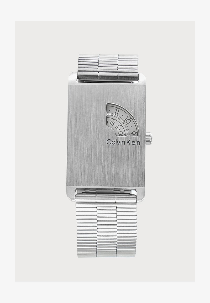 Montre-bracelet argentée Calvin Klein avec cadran rectangulaire, petites fenêtres courbes affichant les heures et les minutes, et bracelet à maillons en métal.