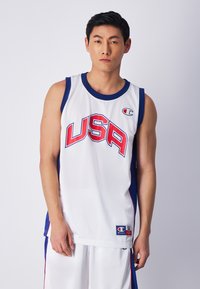 Camiseta de baloncesto blanca con "USA" en letras rojas y azules. Detalles en azul marino en los bordes y en las sisas. Fabricada con tela transpirable.