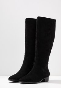 Czarne zamszowe kozaki za kolano o dopasowanym fasonie, spiczastym nosku i niskim, złożonym obcasie; gładka tekstura z bocznymi panelami.
