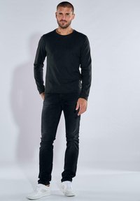 Schwarzes langärmliges Shirt kombiniert mit dunklen Jeans und weißen Sneakern. Das Shirt hat einen runden Ausschnitt und ein körperbetontes Design.
