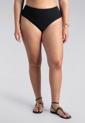 Schwarze hoch taillierte Bikinihosen aus dehnbarem Material, mit glatten Kanten und einem leichten Glanz. Getragen mit schwarzen flachen Sandalen.