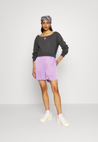 Sweatshirt cinza com design de ombro à mostra e pequeno logo, combinado com calções lilás claros e ténis brancos com detalhes em rosa.