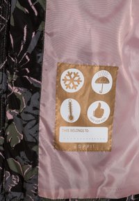 Insidan av flerfärgad blommig jacka har ett rosa foder och en vårdlabel med symboler för temperatur, snö, regn och barnsäkert.