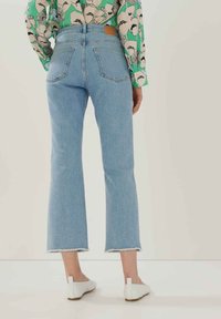 Jeans azzurri chiari a vita alta con gamba dritta, orli sfrangiati e un'etichetta in pelle marrone sulla parte posteriore della vita. Nessuna tasca visibile.