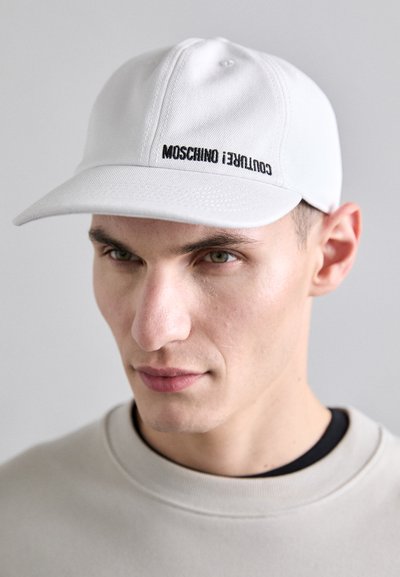 Biała bawełniana czapka z czarnym haftowanym logo "MOSCHINO COUTURE!" z przodu. Płaski daszek i przeszycia wokół korony.