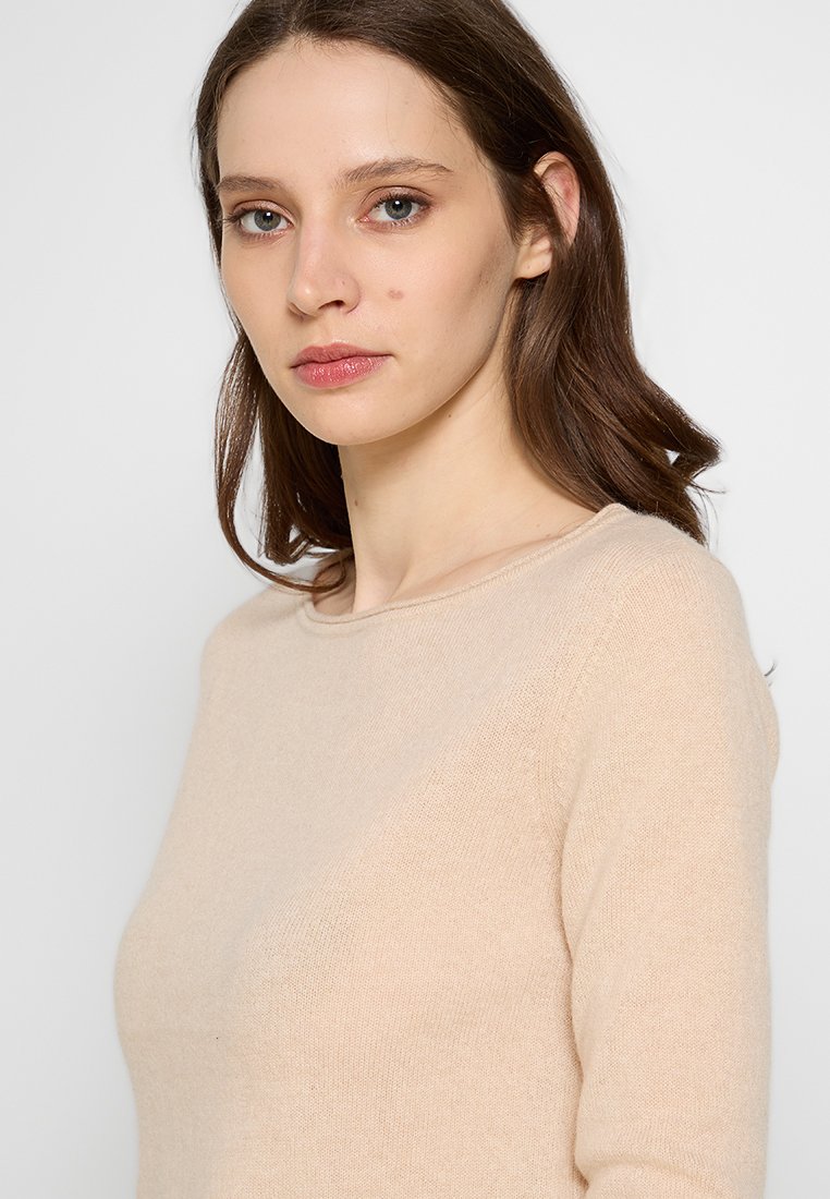 Beige Strickpullover mit rundem Halsausschnitt, langen Ärmeln und weicher Textur. Einfaches Design, minimale Details und taillierte Form.