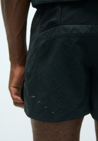 Schwarze Sportshorts mit einem strukturierten Mesh-Einsatz, schlankem Design und reflektierenden Details am Saum. Die Materialien sind leicht und atmungsaktiv.