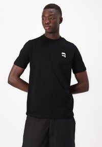 Tricou negru cu maneci scurte, cu decolteu rotund, având un design grafic mic, alb, în partea stângă a pieptului. Fabricat din bumbac.