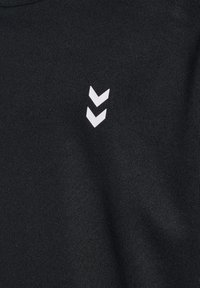 T-shirt en tissu noir avec un logo en chevron blanc sur le côté gauche. Le matériau semble lisse avec un léger éclat.
