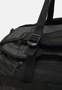Zwarte nylon sporttas met een ritsvak, verstelbare banden en een veilige kliksluiting. Gladde textuur met versterkte stiksels.
