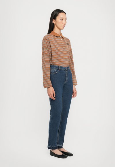 Ριγέ μακρυμάνικο πουκάμισο σε καφέ και πορτοκαλί απόχρωση, συνδυασμένο με μπλε τζιν ψηλής μέσης. Μαύρες μπαλαρίνες και ίσια γραμμή ολοκληρώνουν την εμφάνιση.