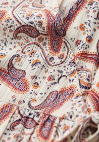 Tela ligeramente texturizada en crema con un patrón de paisley en tonos de azul, rojo y naranja. Presenta detalles gathered y sutiles acentos florales.