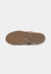 Sole of a sneaker featuring a herringbone tread pattern, with a small logo on the heel and a light-colored upper edge.