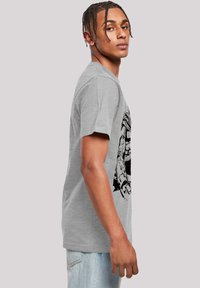 Grå bomulls t-skjorte med et svart grafisk design på fronten. Korte ermer og en avslappet passform. Denim jeans er synlige nederst.