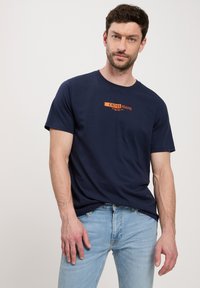 Granatowa bawełniana koszulka z krótkim rękawem, z okr ągłym dekoltem, z czerwoną i pomarańczową grafiką logo na przodzie.