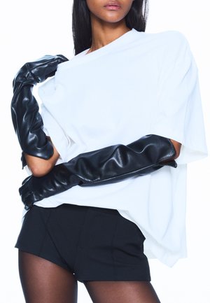 Czarne długie rękawiczki z ekoskóry, oversize'owa biała koszulka i czarne spodenki. Gładka faktura, luźny krój, z warstwowym detalem na ramieniu.