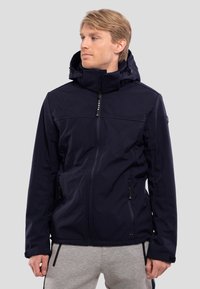 Laijava navy-softshell takki, jossa on täysi vetoketju, säädettävä huppu, vetoketjulliset taskut ja joustavat hihansuut. Takki on sileä ja minimalistinen muotoilu.