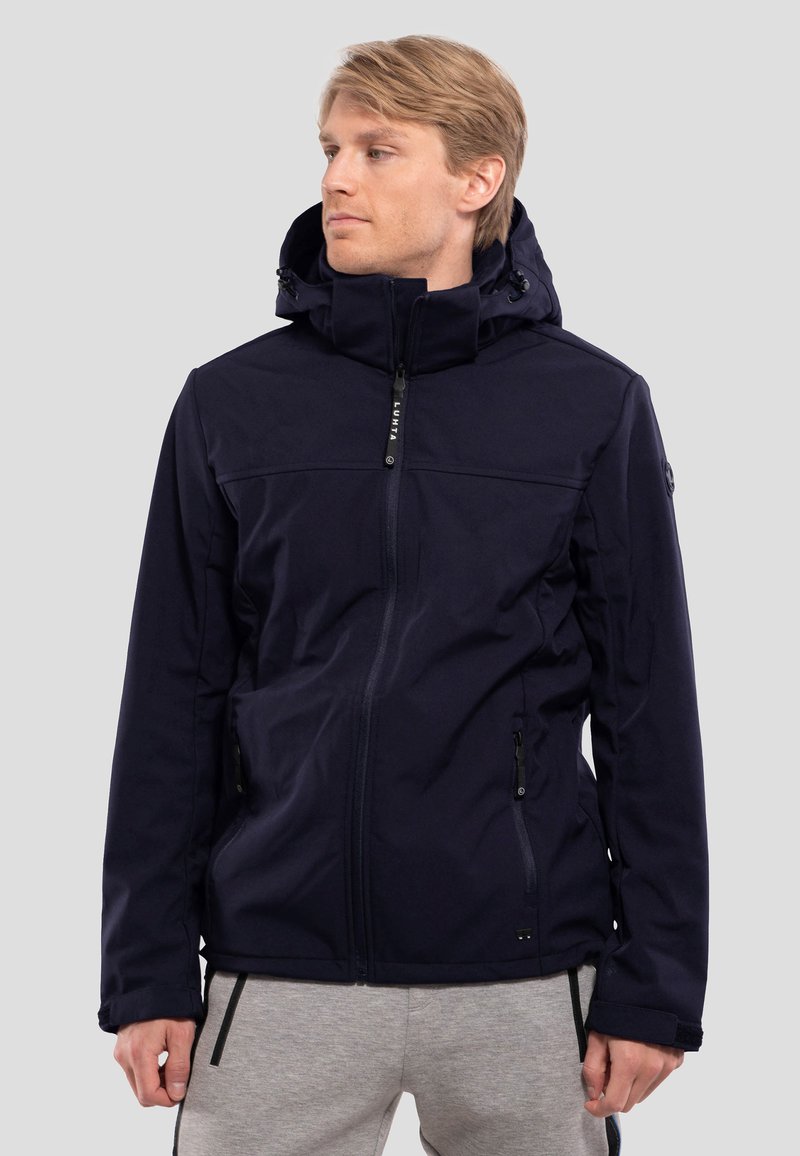 Laijava navy-softshell takki, jossa on täysi vetoketju, säädettävä huppu, vetoketjulliset taskut ja joustavat hihansuut. Takki on sileä ja minimalistinen muotoilu.