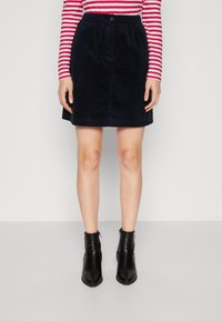 Falda de pana marina con cinturilla elástica, botón en el frente, diseño hasta la rodilla, combinada con botas negras de tobillo, textura de cuero suave.