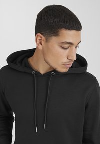 Black hoodie made of cotton blend fabric, featuring a drawstring hood, ribbed cuffs, and a smooth texture. Close-up view focusing on design.