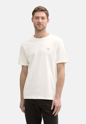 White cotton T-shirt with a crew neckline and short sleeves. Features a small circular logo on the left chest. Simple design, relaxed fit.