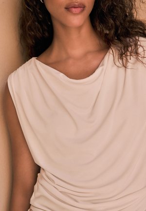 Top beige drappeggiato con una texture morbida e liscia. Presenta un collo a cisterna e dettagli arricciati in vita, che accentuano la silhouette.