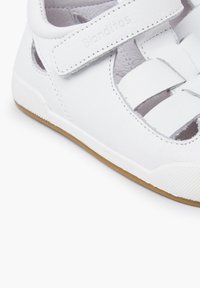Weiße Ledersandalen mit einem Velcro-Riemen, Ausschnitten an den Seiten und einer strukturierten gummiartigen Sohle in Tan. Mit einem geflochtenen Design auf dem Obermaterial.