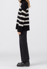 Pull à col roulé en maille douce rayé noir et blanc avec une coupe ample, associé à un pantalon noir évasé et des bottines.