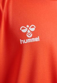 Leuchtend orange Sporttrikot aus strukturiertem Stoff, ausgestattet mit einem weißen "Hummel"-Logo und einem stilisierten Bienenmuster.